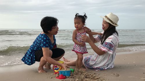 Smiling mother sitting with baby girl playing on shore at beach