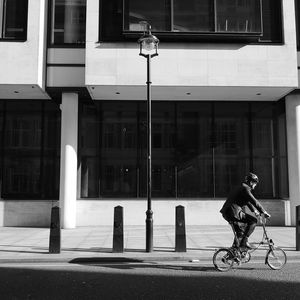 Man riding bicycle on street against building in city