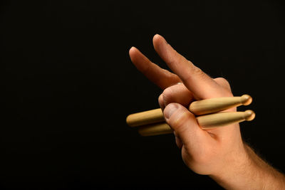 Cropped hand gesturing drumsticks against black background