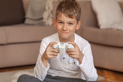 Portrait of boy holding video game remote control in living room at home 