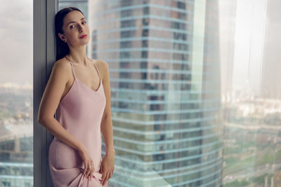 Woman in a nightgown stands at the window in a skyscraper near the bed