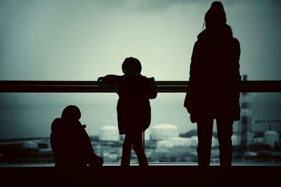 Rear view of silhouette woman with children on bridge at dusk