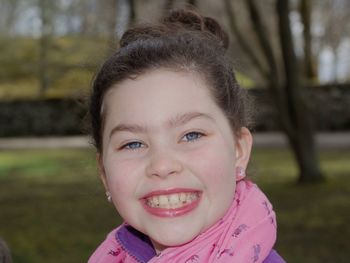 Close-up portrait of smiling girl with blue eyes standing at park