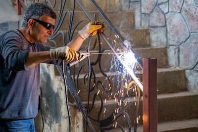 Man wearing protective glasses welds metal with welding machine. sparks from welding fly to sides.