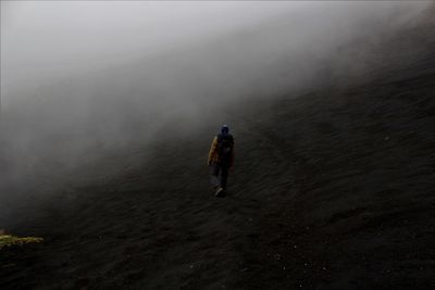 Rear view of man walking on land during foggy weather