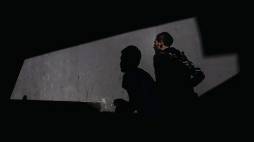 Silhouette friends standing against wall at night