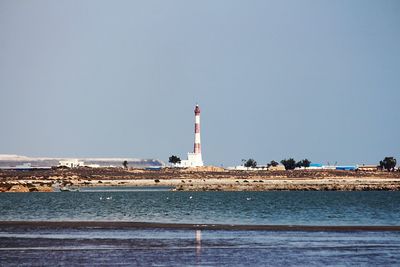 Lighthouse by sea against clear sky