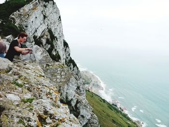 Man standing on cliff by sea against sky