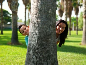 Portrait of smiling young woman holding tree trunk in park