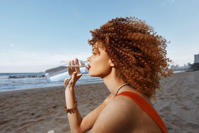 Young woman drinking water at beach