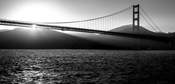 Golden gate bridge over sea against sun at sunset