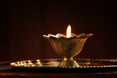 Close-up of illuminated oil lamp on table against wall