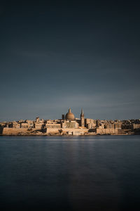 View of buildings by river against sky in city