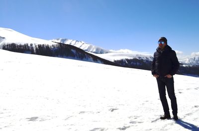 Full length of man standing on snowcapped mountain against sky