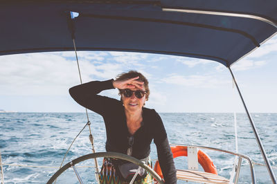 Portrait of smiling mature woman standing in boat on sea