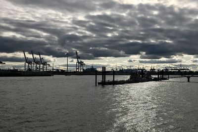 Pier at harbor against cloudy sky