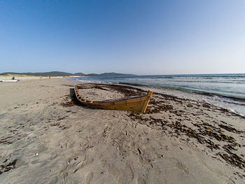 Deck chairs on sand at beach against clear sky