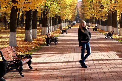 Full length portrait of woman standing on footpath in park during autumn