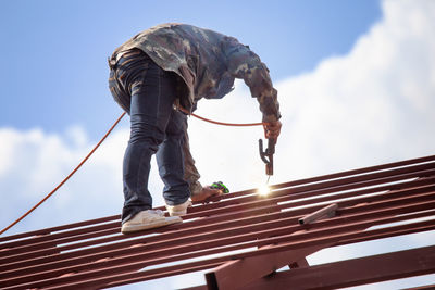 Low angle view of man working on roof against sky