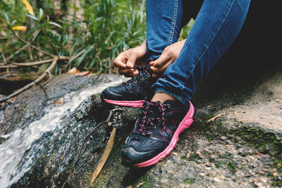 Low section of man tying shoelace while sitting on rock