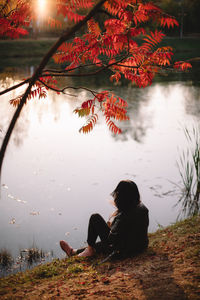 Young woman sitting by lake under a tree during autumn