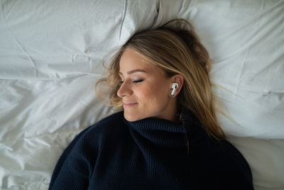 Woman listens to music with headphones in her bed in her apartment. mobile phone, technology.