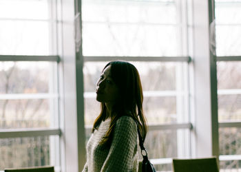 Side view of woman standing by window