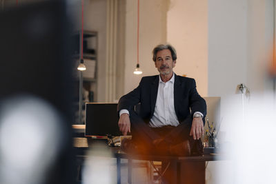 Senior businessman sitting cross-legged on desk in office