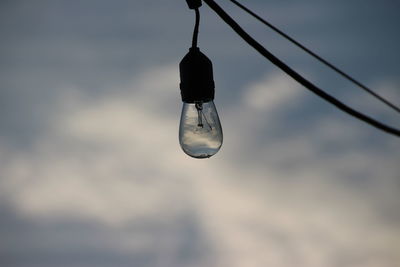 Close-up of water drop hanging against sky