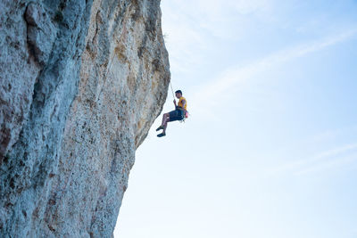 Low angle view of man climbing rock against sky