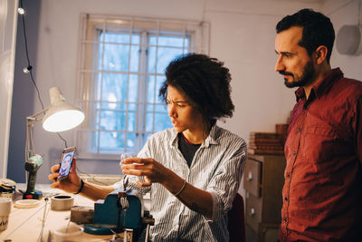 Technician with coworker showing light bulb to engineer through video conferencing on mobile phone