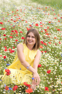 A beautiful young blonde woman in a yellow dress stands among a flowering field