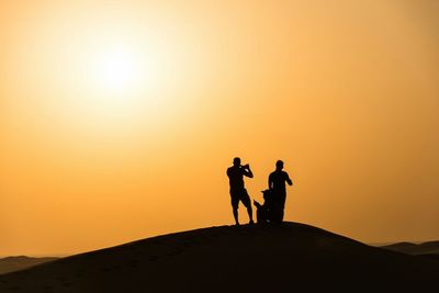 Silhouette men standing on desert during sunset