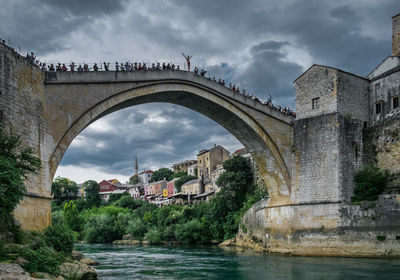 Arch bridge over river amidst buildings against sky