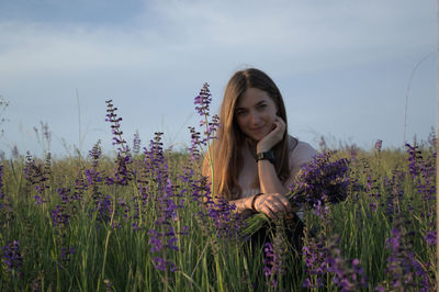 Portrait of young woman standing amidst plants against sky