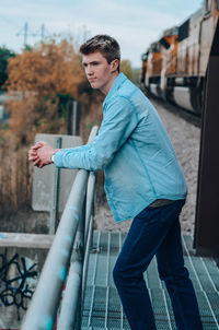 Side view of young man standing against railing in city