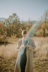 A young woman using her phone in a field during a sunny autumn day