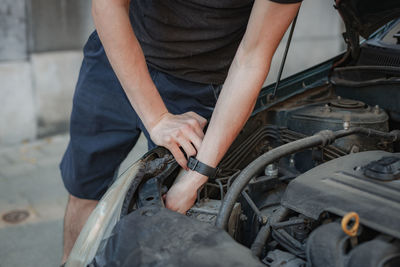 A young man takes out a headlight bulb from the open hood of a car.