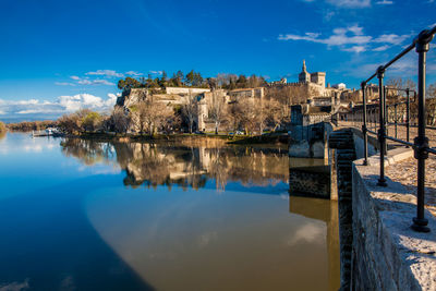 Arch bridge over river by buildings against blue sky