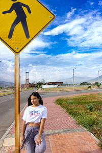 Portrait of teenage girl standing by road sign on footpath 