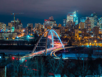 Illuminated bridge and buildings against sky at night