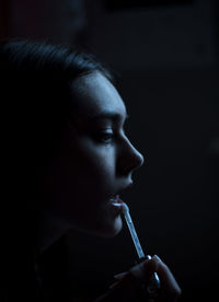 Close-up of young woman applying lipstick in dark