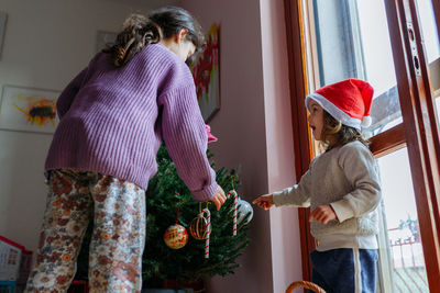 Low angle view on two sisters decorating christmas tree in their home