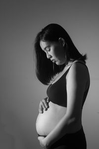 Side view of young pregnant woman against gray background