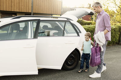 Father and son standing by car with open doors and trunk on street