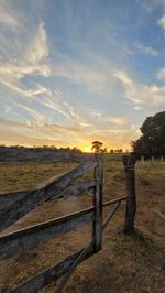 Wooden fence on field against sky during sunset