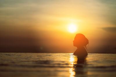 Silhouette woman in infinity pool during sunset