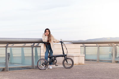 Young woman looking at camera leaning on an electric bicycle in the city with copy space around.