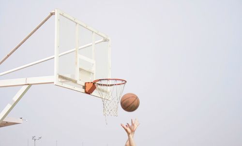 Cropped image of hands throwing on basketball on hoop against sky 