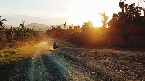 Man riding motorcycle on dirt road against sky